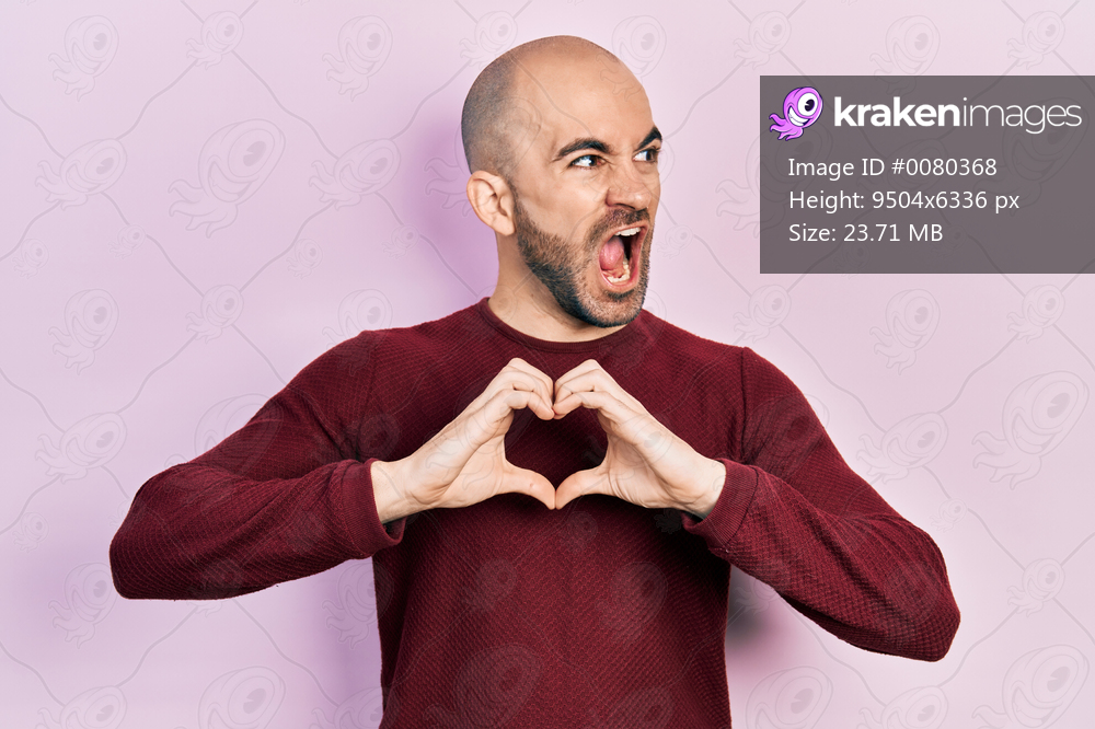 Young bald man doing heart symbol with hands angry and mad screaming frustrated and furious, shouting with anger. rage and aggressive concept. 