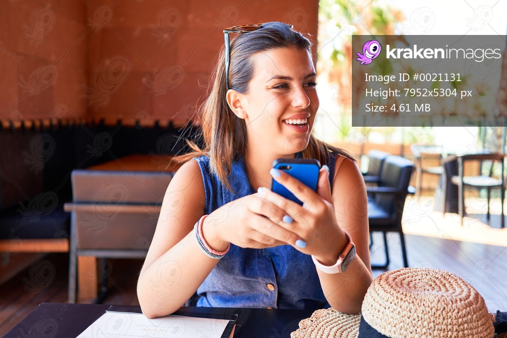 Young beautiful woman sitting at restaurant enjoying summer vacation using smartphone