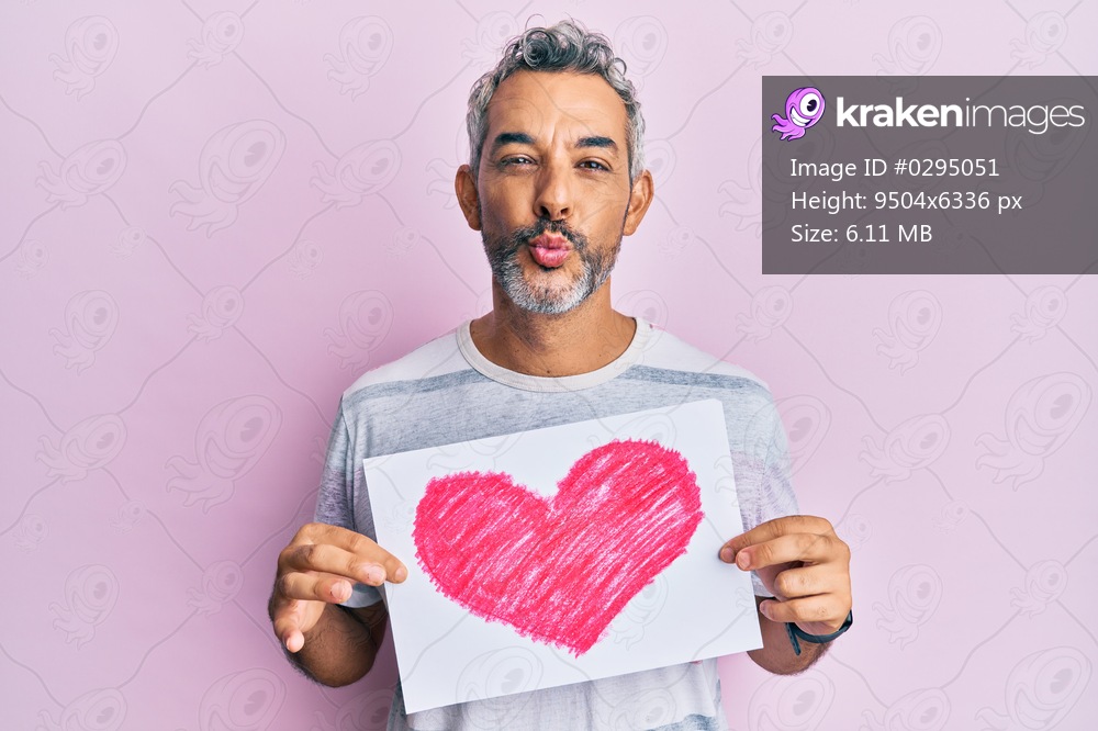 Middle age grey-haired man holding heart draw looking at the camera blowing a kiss being lovely and sexy. love expression. 