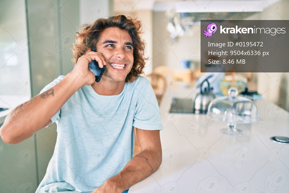 Young hispanic man smiling happy talking on the smartphone sitting on the table at home