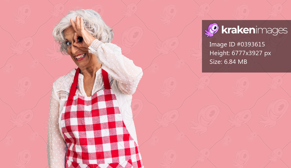Senior grey-haired woman wearing apron smiling happy doing ok sign with hand on eye looking through fingers 