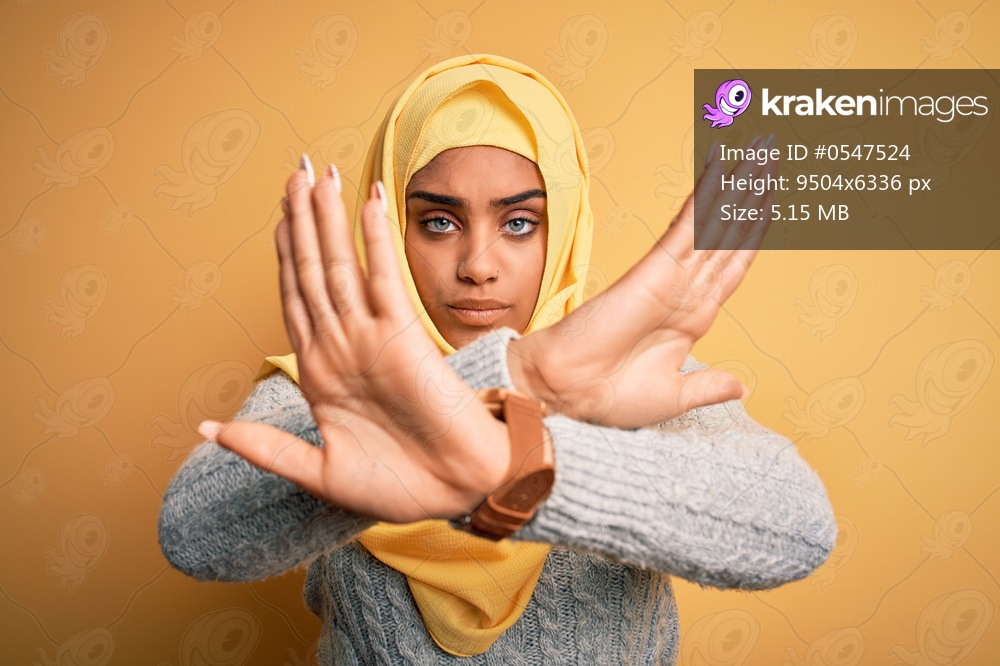 Young beautiful african american girl wearing muslim hijab over isolated yellow background Rejection expression crossing arms doing negative sign, angry face