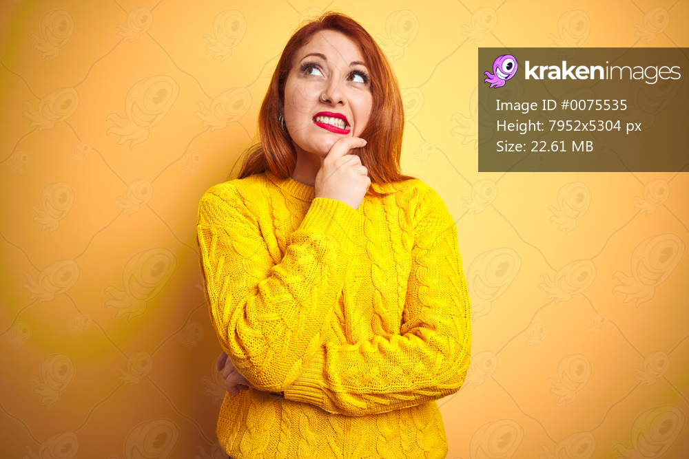 Beautiful redhead woman wearing winter sweater standing over isolated yellow background Thinking worried about a question, concerned and nervous with hand on chin