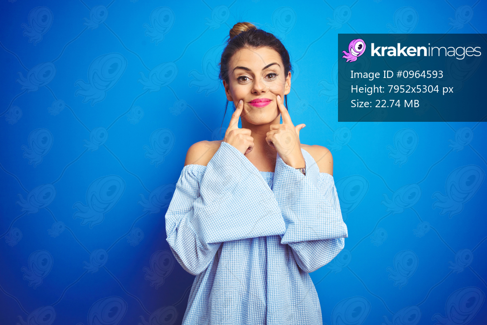 Young beautiful woman wearing bun hairstyle over blue isolated background Smiling with open mouth, fingers pointing and forcing cheerful smile