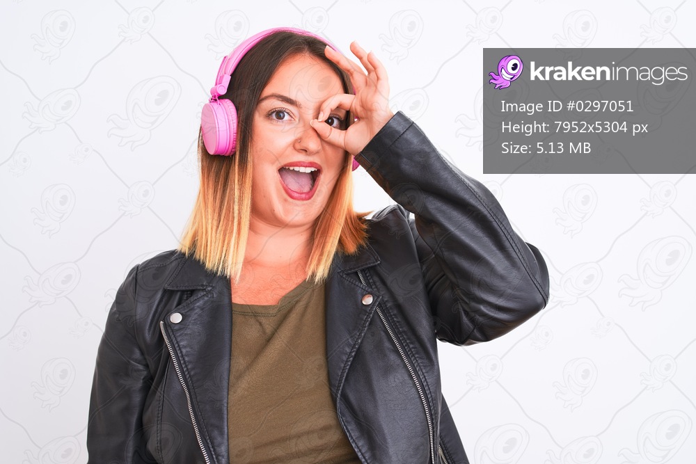 Young beautiful woman listening to music using headphones over isolated white background doing ok gesture with hand smiling, eye looking through fingers with happy face.