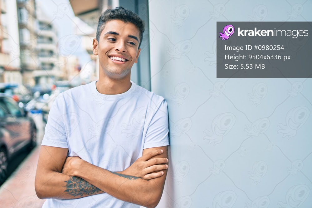 Young latin man smiling happy leaning on the wall at the city.