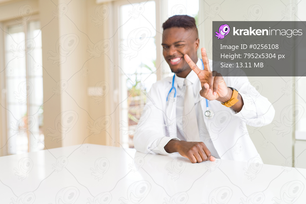 African american doctor man at the clinic smiling looking to the camera showing fingers doing victory sign. Number two.