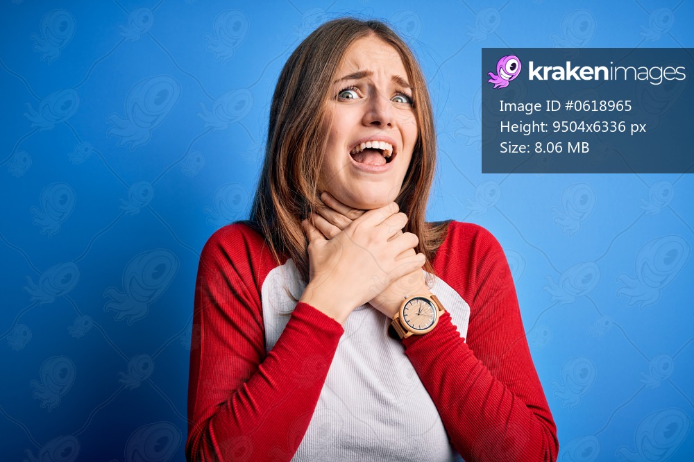 Young beautiful redhead woman wearing casual t-shirt over isolated blue background shouting and suffocate because painful strangle. Health problem. Asphyxiate and suicide concept.