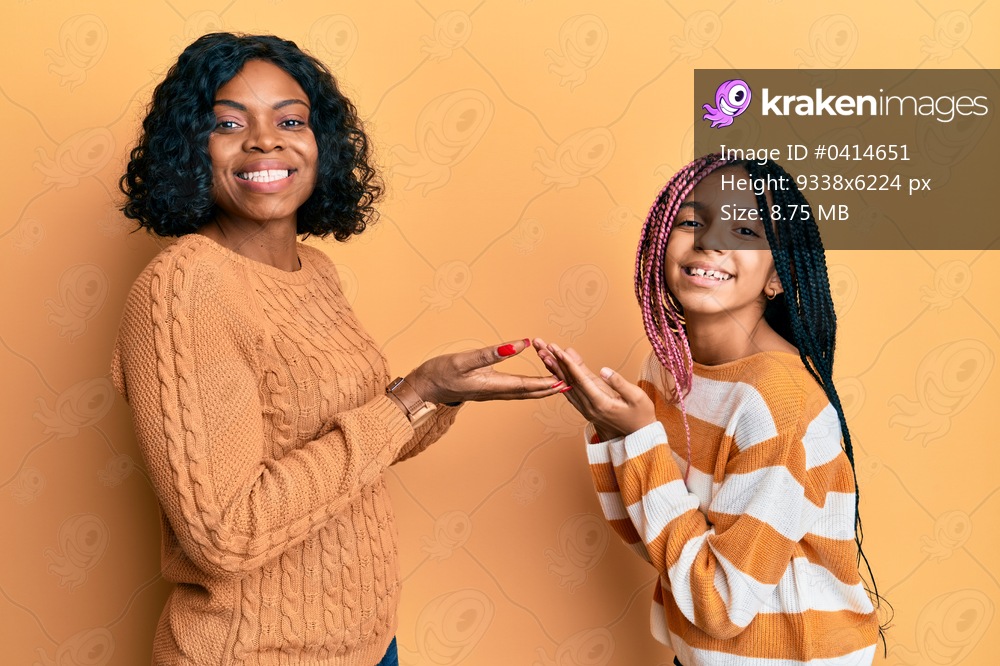 Beautiful african american mother and daughter wearing wool winter sweater pointing aside with hands open palms showing copy space, presenting advertisement smiling excited happy 
