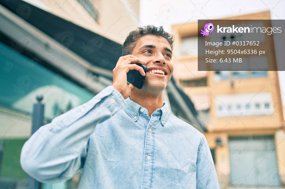 Young latin man smiling happy talking on the smartphone walking at the city.