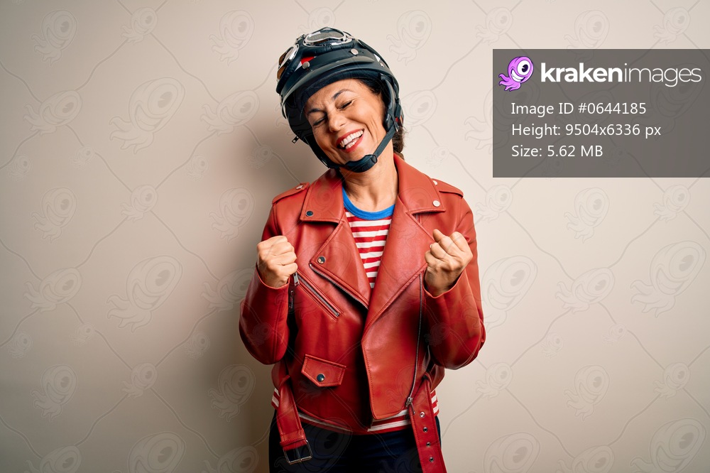 Middle age motorcyclist woman wearing motorcycle helmet and jacket over white background very happy and excited doing winner gesture with arms raised, smiling and screaming for success. Celebration concept.