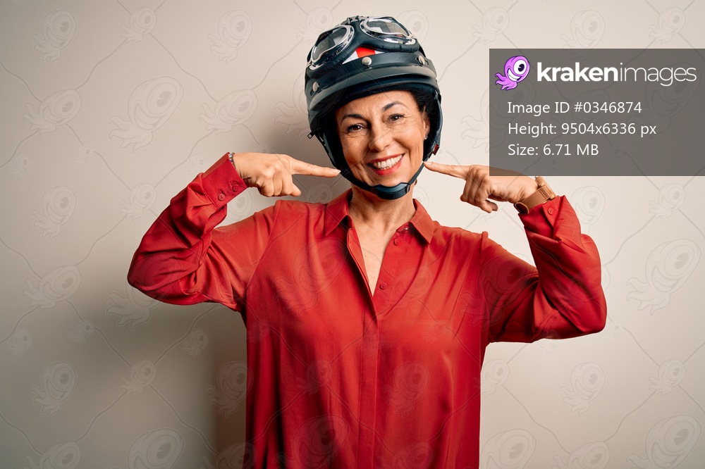 Middle age motorcyclist woman wearing motorcycle helmet over isolated white background smiling cheerful showing and pointing with fingers teeth and mouth. Dental health concept.
