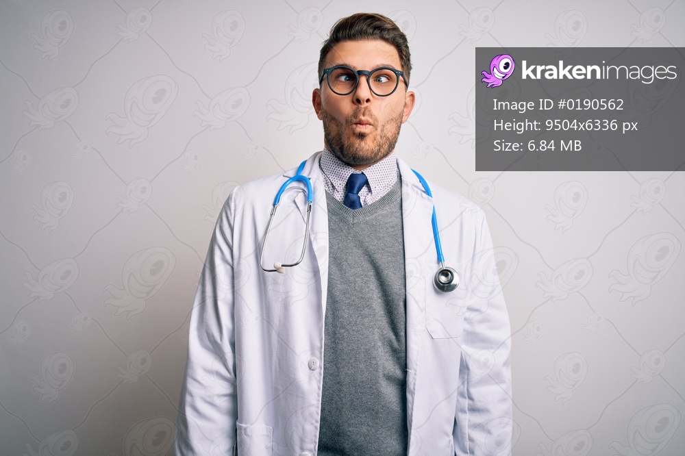 Young doctor man with blue eyes wearing medical coat and stethoscope over isolated background making fish face with lips, crazy and comical gesture. Funny expression.