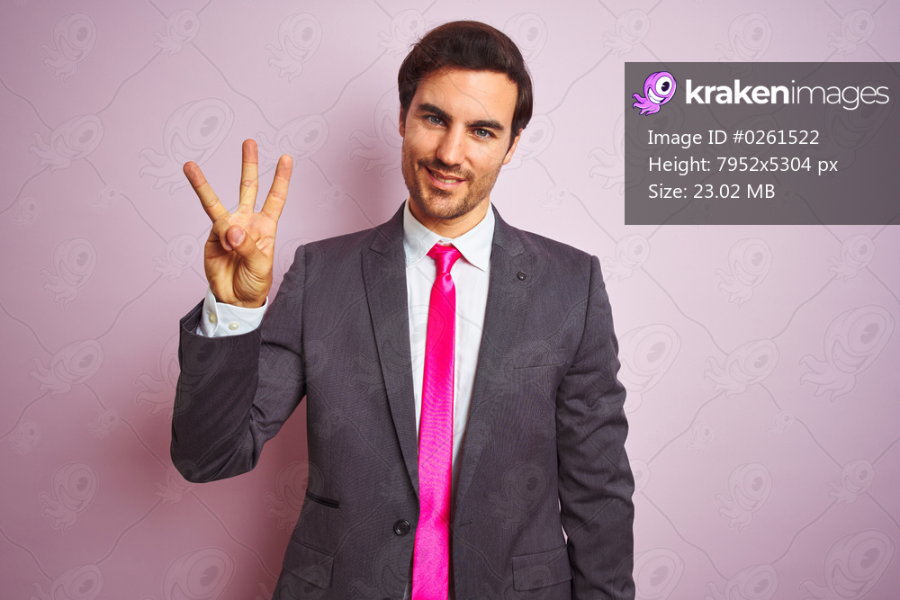 Young handsome businessman wearing suit and tie standing over isolated pink background showing and pointing up with fingers number three while smiling confident and happy.