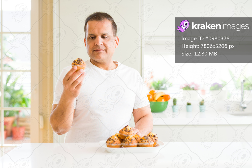 Middle age man eating chocolate chip muffins at home with a confident expression on smart face thinking serious