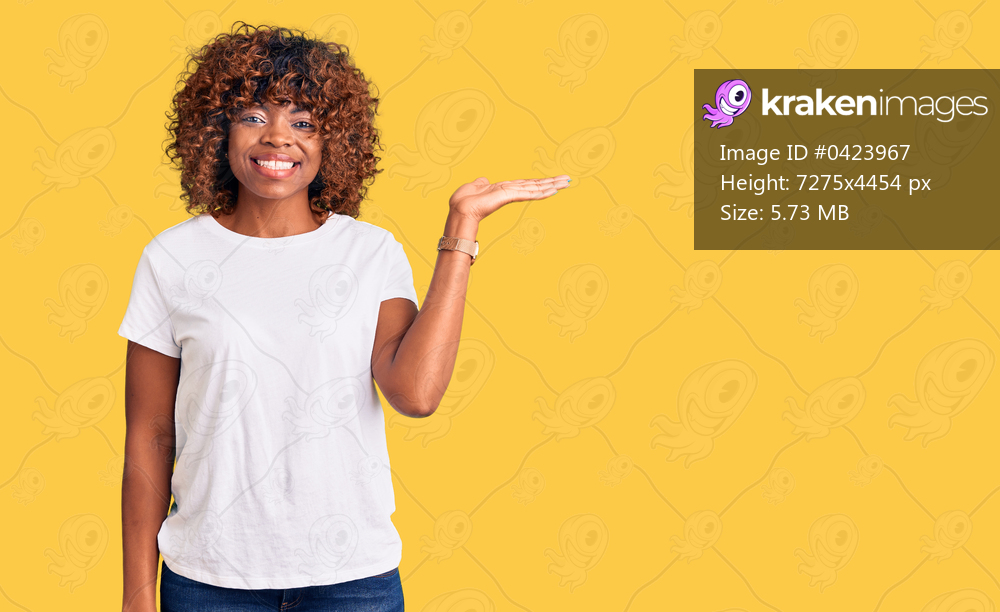 Young african american woman wearing casual white tshirt smiling cheerful presenting and pointing with palm of hand looking at the camera. 