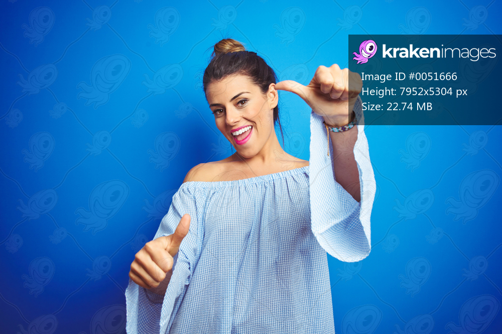 Young beautiful woman wearing bun hairstyle over blue isolated background approving doing positive gesture with hand, thumbs up smiling and happy for success. Winner gesture.