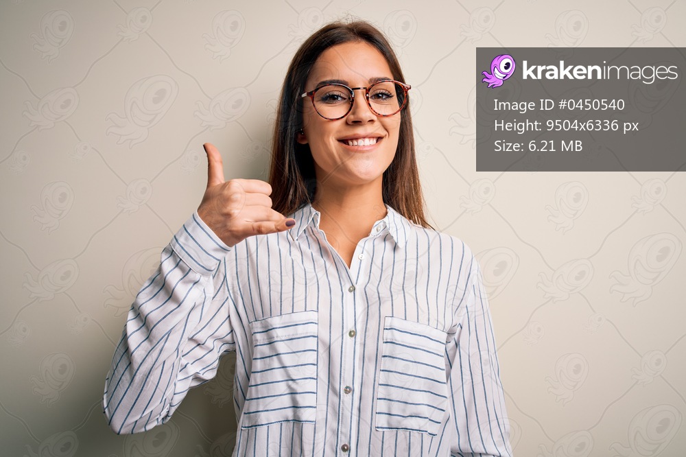 Young beautiful brunette woman wearing casual shirt and glasses over white background smiling doing phone gesture with hand and fingers like talking on the telephone. Communicating concepts.