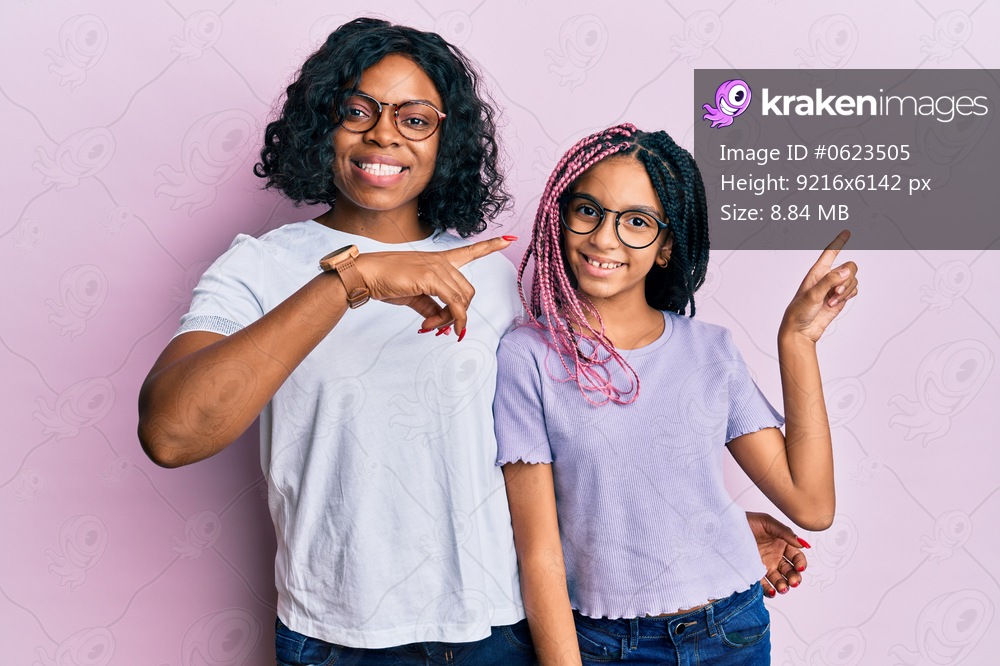 Beautiful african american mother and daughter wearing casual clothes and glasses smiling and looking at the camera pointing with two hands and fingers to the side. 