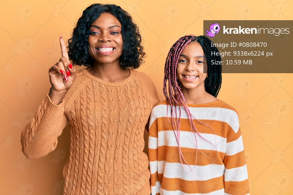 Beautiful african american mother and daughter wearing wool winter sweater showing and pointing up with finger number one while smiling confident and happy. 