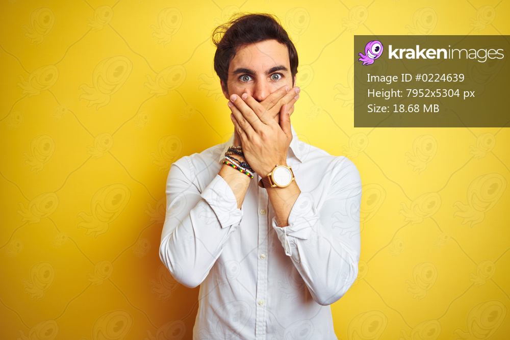 Young handsome businessman wearing elegant shirt standing over isolated yellow background shocked covering mouth with hands for mistake. Secret concept.