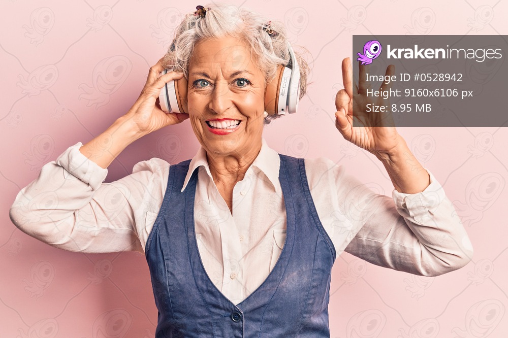 Senior grey-haired woman listening to music using headphones doing ok sign with fingers, smiling friendly gesturing excellent symbol 