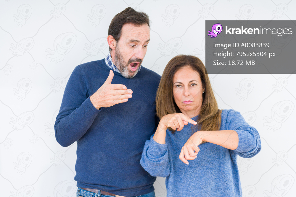 Beautiful middle age couple in love over isolated background In hurry pointing to watch time, impatience, upset and angry for deadline delay