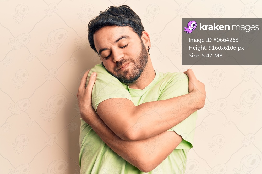 Young hispanic man wearing casual clothes hugging oneself happy and positive, smiling confident. self love and self care 