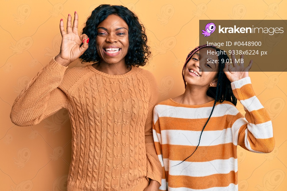 Beautiful african american mother and daughter wearing wool winter sweater smiling positive doing ok sign with hand and fingers. successful expression. 