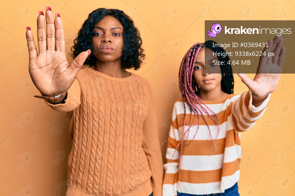Beautiful african american mother and daughter wearing wool winter sweater doing stop sing with palm of the hand. warning expression with negative and serious gesture on the face. 
