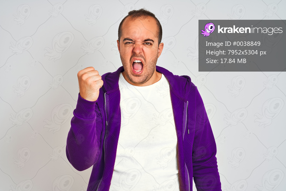 Young man wearing purple sweatshirt standing over isolated white background angry and mad raising fist frustrated and furious while shouting with anger. Rage and aggressive concept.