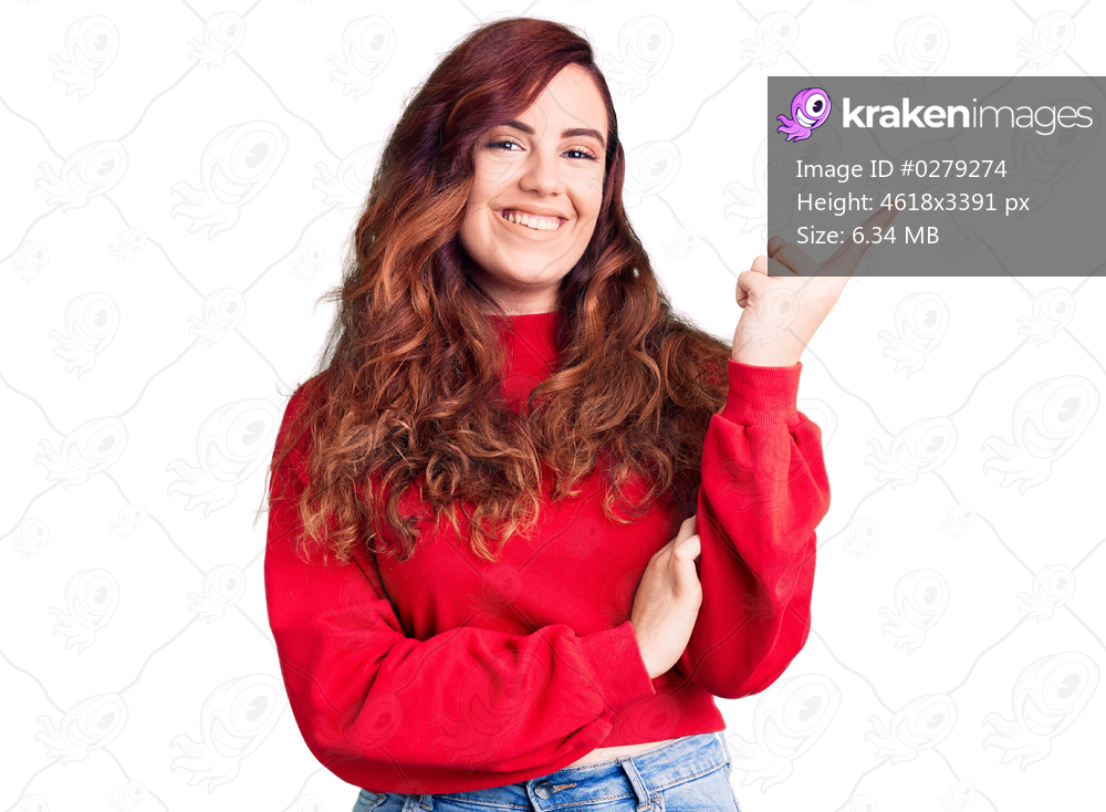 Young beautiful woman wearing casual winter sweater with a big smile on face, pointing with hand and finger to the side looking at the camera. 