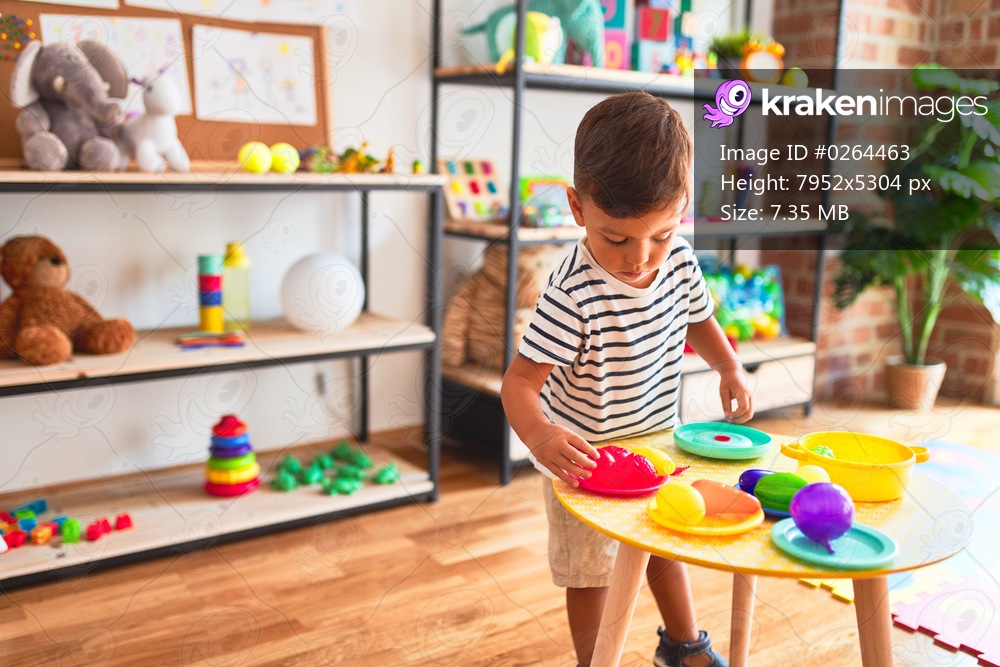 Beautiful toddler boy playing meals with plastic plates, fruits and vegetables at kindergarten
