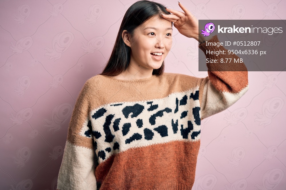 Young beautiful asian woman wearing animal print fashion sweater over pink isolated background very happy and smiling looking far away with hand over head. Searching concept.