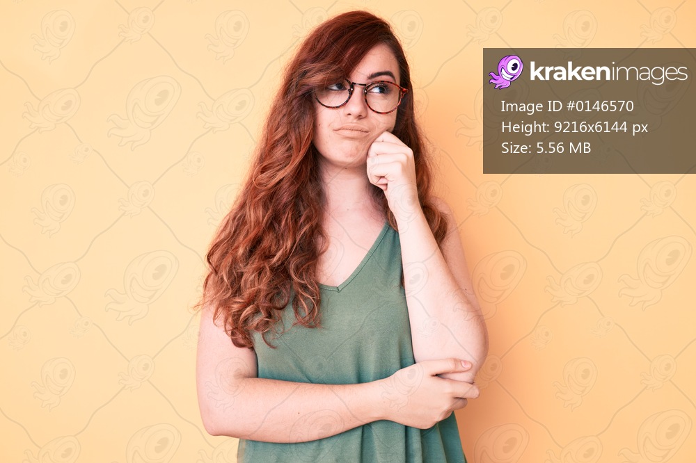 Young beautiful woman wearing casual clothes and glasses serious face thinking about question with hand on chin, thoughtful about confusing idea 