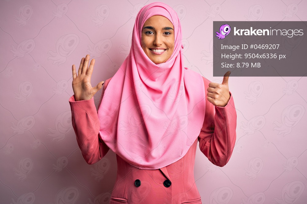 Young beautiful brunette businesswoman wearing pink muslim hijab and business jacket showing and pointing up with fingers number six while smiling confident and happy.