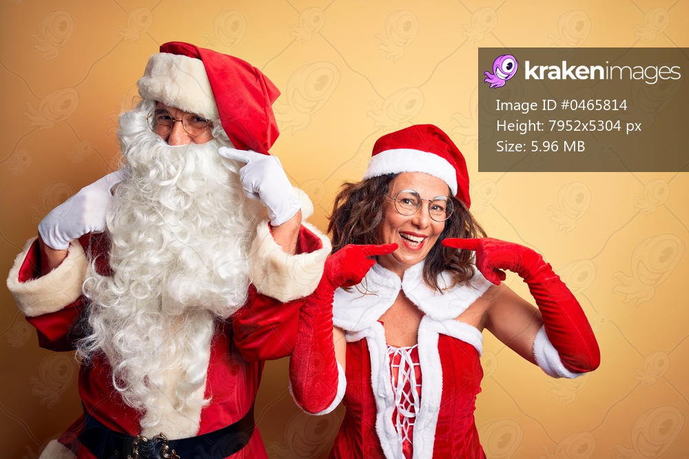 Middle age couple wearing Santa costume and glasses over isolated yellow background smiling cheerful showing and pointing with fingers teeth and mouth. Dental health concept.