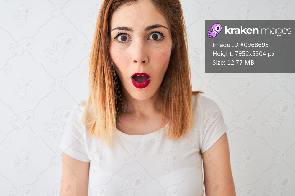 Beautiful redhead woman wearing casual t-shirt standing over isolated white background scared in shock with a surprise face, afraid and excited with fear expression