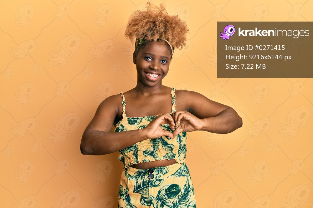 Young african woman with afro hair wearing summer dress smiling in love doing heart symbol shape with hands. romantic concept. 