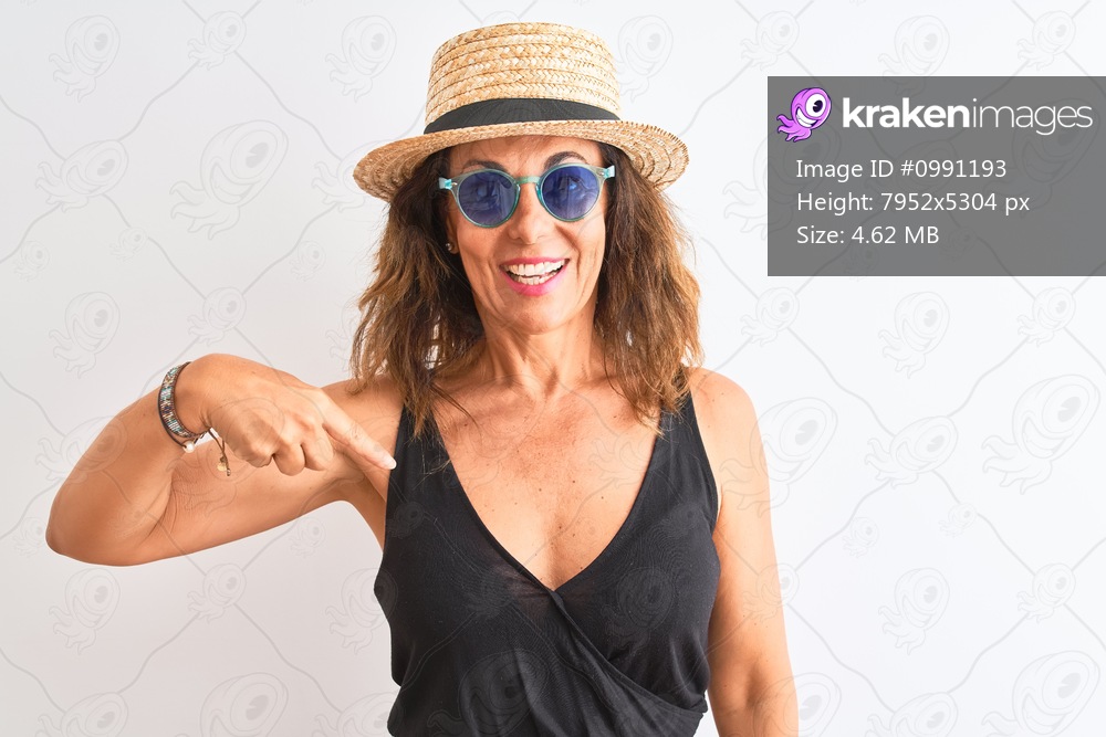 Middle age woman wearing black t-shirt sunglasses and hat over isolated white background with surprise face pointing finger to himself