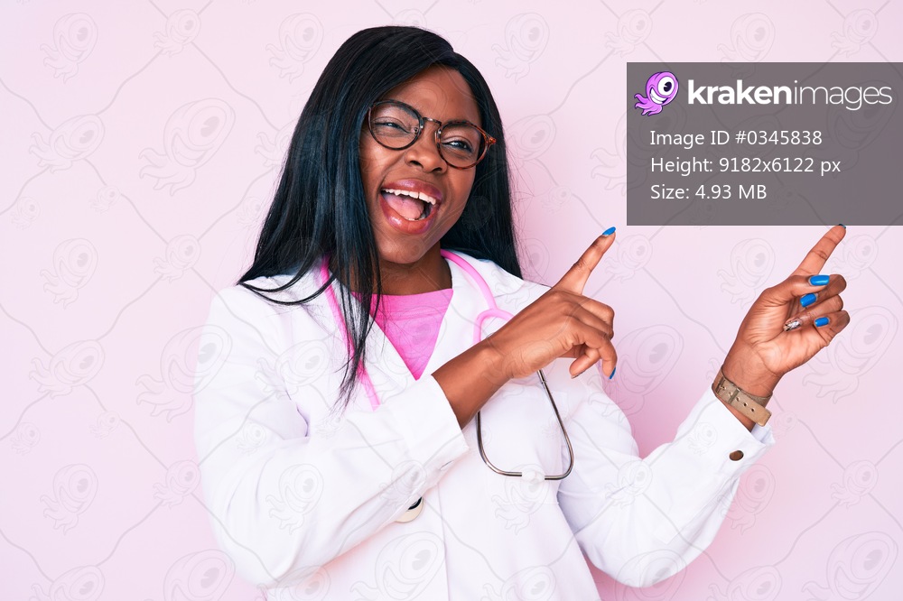 Young african american woman wearing doctor stethoscope smiling and looking at the camera pointing with two hands and fingers to the side. 