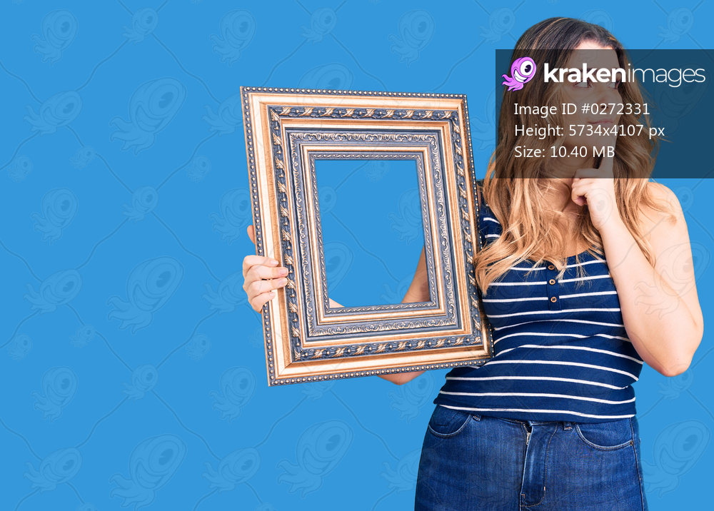 Young caucasian woman holding empty frame serious face thinking about question with hand on chin, thoughtful about confusing idea 
