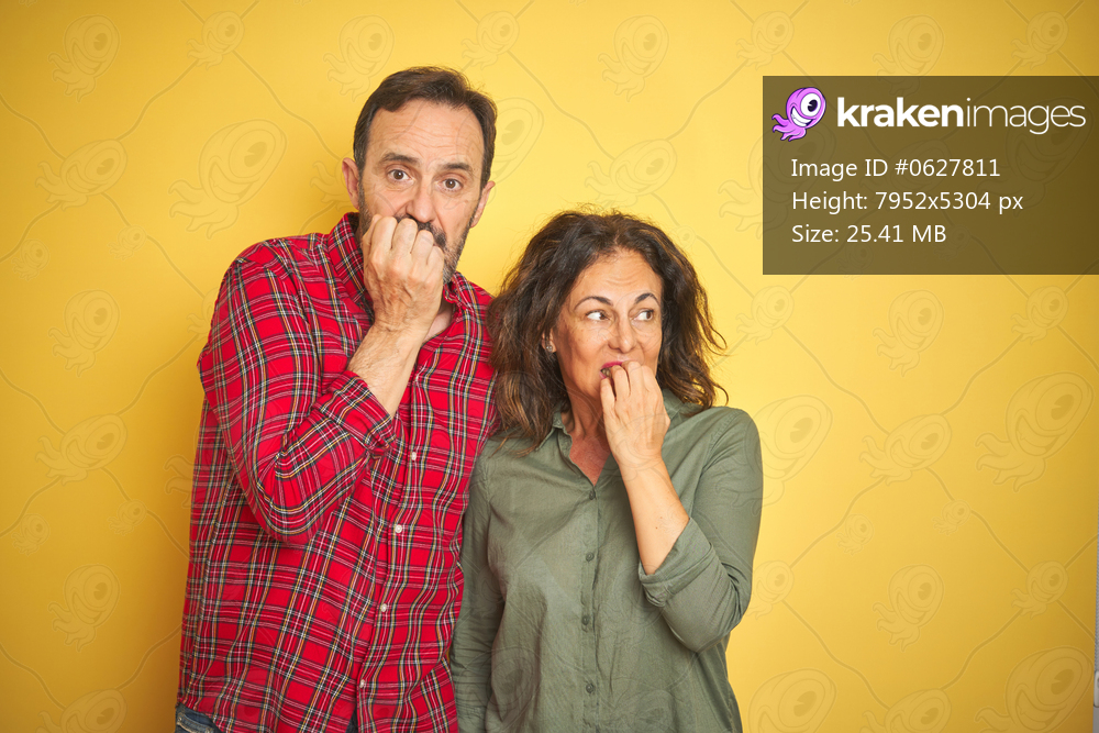Beautiful middle age couple over isolated yellow background looking stressed and nervous with hands on mouth biting nails. Anxiety problem.