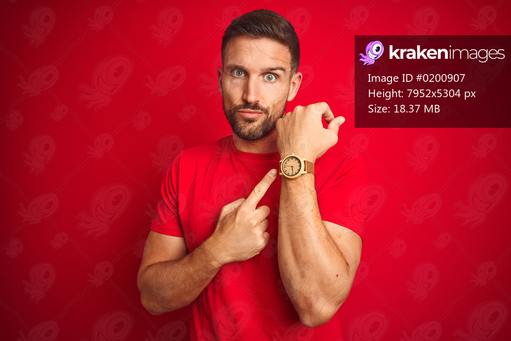 Young handsome man wearing casual t-shirt over red isolated background In hurry pointing to watch time, impatience, looking at the camera with relaxed expression