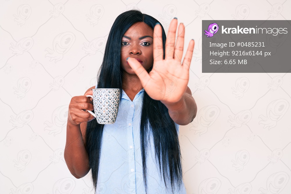 Young african american woman holding coffee with open hand doing stop sign with serious and confident expression, defense gesture 