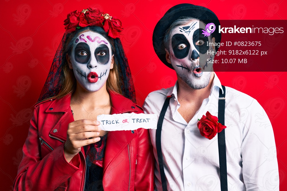 Couple wearing day of the dead costume holding trick or treat paper scared and amazed with open mouth for surprise, disbelief face 