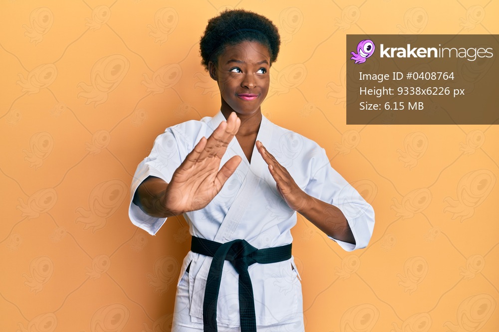 Young african american girl wearing karate kimono and black belt smiling looking to the side and staring away thinking. 