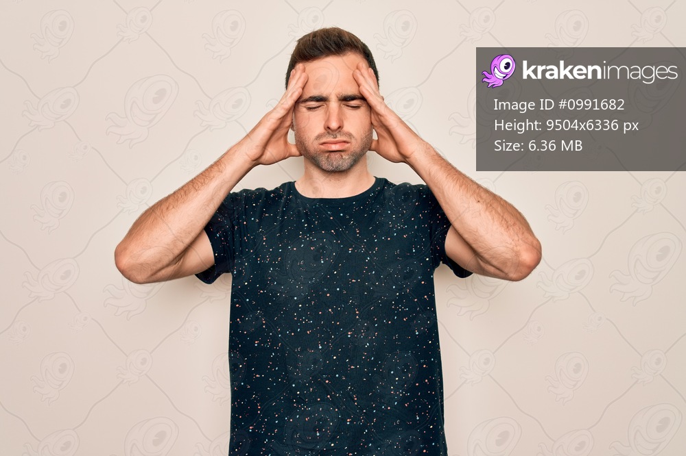 Young handsome man with blue eyes wearing casual t-shirt standing over white background suffering from headache desperate and stressed because pain and migraine. Hands on head.