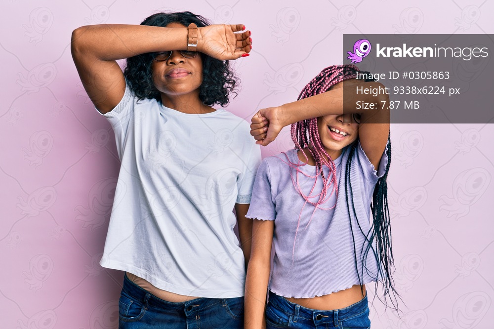 Beautiful african american mother and daughter wearing casual clothes and glasses covering eyes with arm smiling cheerful and funny. blind concept. 