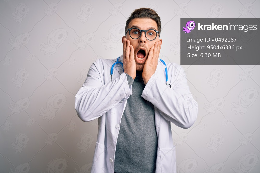 Young doctor man with blue eyes wearing medical coat and stethoscope over isolated background afraid and shocked, surprise and amazed expression with hands on face